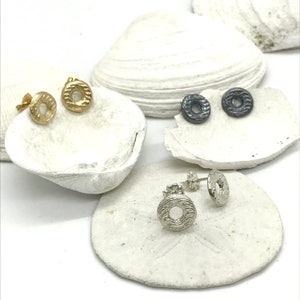 May include: Three pairs of small, textured, circular earrings. One pair is gold, one pair is silver, and one pair is black.