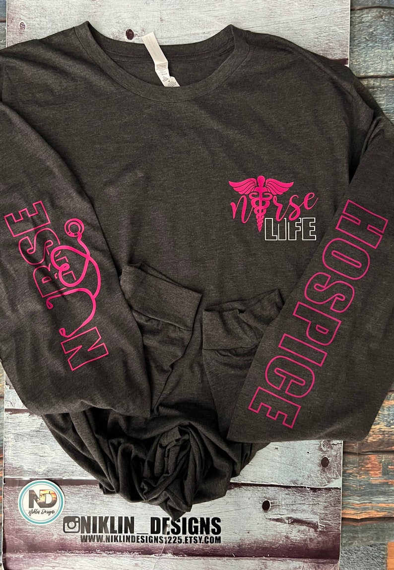 May include: A dark gray long-sleeved shirt with pink text on the sleeves and front. The text on the sleeves reads "HOSPITAL" and "NURSE". The text on the front reads "NURSE LIFE" with a caduceus symbol.