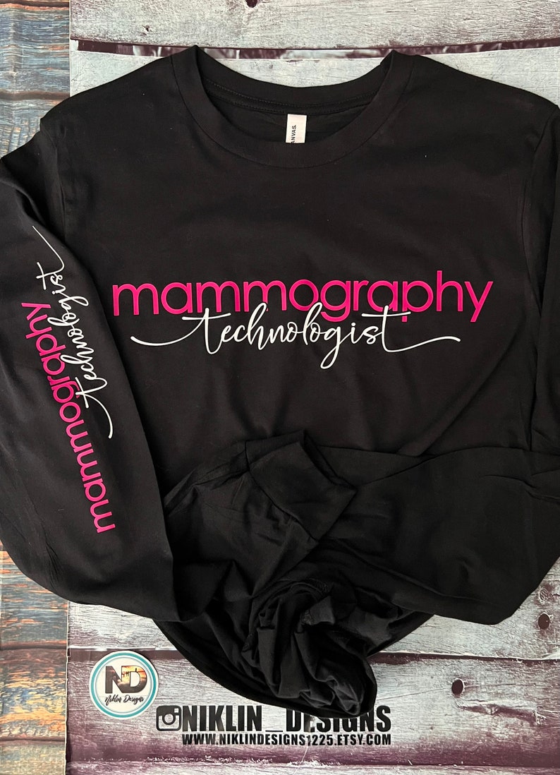 Op de afbeelding: Zwart longsleeve shirt met roze tekst die "mammography technologist" op de voorkant staat en dezelfde tekst verticaal op de linkermouw.