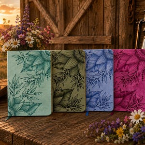 May include: Four journals with sunflower and leaf designs in shades of teal, olive green, blue, and magenta. The journals are on a rustic wooden table with a bouquet of flowers and a lantern in the background.