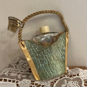 May include: A vintage perfume bottle in a small, green and gold, fabric-covered basket with a rope handle. The label on the bottle reads "Gardenias by Karyl, Conc. 1/4 oz."