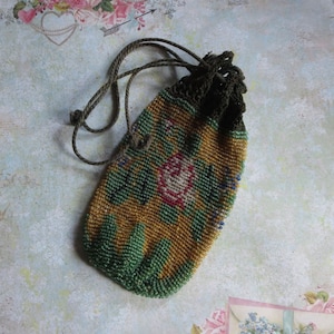 May include: A small drawstring pouch crafted from tiny glass beads in shades of mustard yellow, forest green, and rose pink. The bag features a floral pattern and a dark green crocheted top section with matching thin cord drawstrings for closure.