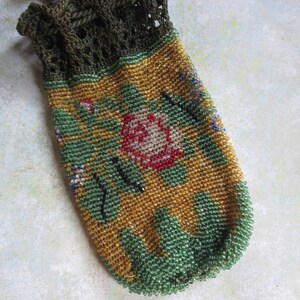 May include: A drawstring pouch featuring a dark olive green crocheted top and a body covered in intricate glass beads. The beadwork displays a floral pattern with a central pink rose, green leaves, and a golden yellow background with green trim.