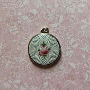 May include: A silver locket with a white enamel background and a hand-painted pink rose with green leaves.