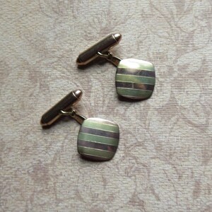 May include: A pair of gold cufflinks with a striped design. The cufflinks are rectangular and have a polished finish.