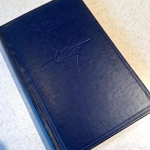 May include: A navy blue book with the embossed word "Ottawa" in a script font. The book has a textured cover and a rectangular border design. The edges of the book are dark blue.