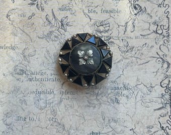 May include: A black and silver octagonal brooch with a black and white floral design in the center.