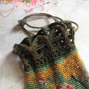May include: A small drawstring pouch featuring a dark olive green crocheted top section with a matching cord closure. The lower portion of the pouch is covered in intricate, multi-colored glass seed beads in shades of gold, green, and red.