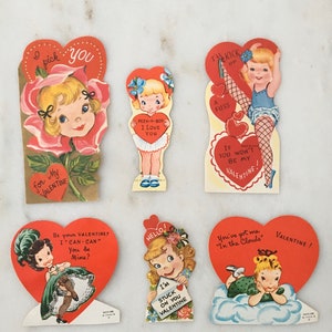 May include: Five vintage Valentine's Day cards featuring illustrations of girls with hearts and flowers. The cards are printed on thick paper and have a red, white, and pink color scheme.