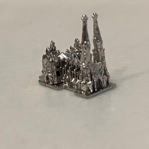 May include: A miniature silver replica of the Sagrada Familia basilica. The detailed model features the iconic spires and architectural elements of the famous Barcelona landmark. The miniature is a detailed representation of the cathedral.