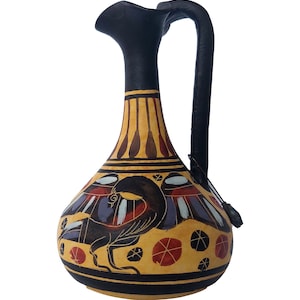 May include: A black and yellow ceramic pitcher with a bird design. The pitcher has a wide base and a narrow neck with a handle.