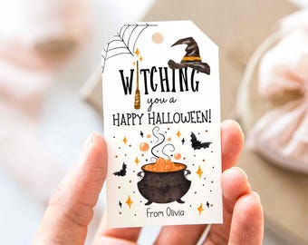Op de afbeelding: Een witte Halloween-cadeaulabel met de woorden "Witching you a Happy Halloween!" in het zwart. De label heeft een heksenhoed, een ketel, vleermuizen en een spinnenwebontwerp. De label is gepersonaliseerd met de naam "Olivia".