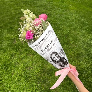 May include: A bouquet of pink and white flowers wrapped in a newspaper cone with the text "Die Muttertagszeitung" and "Du bist die Beste Mama der Welt".
