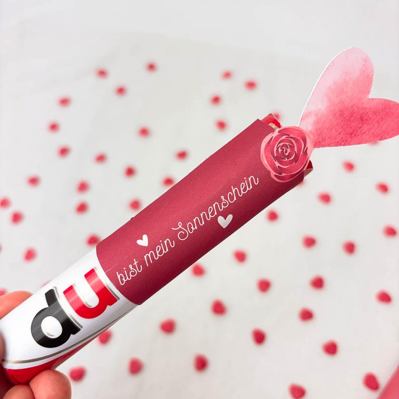 Pu&ograve; includere: Un tubo di caramelle rosso e bianco con la parola "du" in lettere rosse. Il tubo &egrave; avvolto in carta rosso scuro con le parole "bist mein Sonnenschein" e un simbolo di cuore. Sono attaccate una rosa e un cuore di carta.