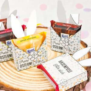 Puede incluir: Cajas de regalo de Pascua con barras de chocolate, dise&ntilde;os florales y orejas de conejo de papel. Las cajas tienen el texto "Frohe OSTERN!" y "HASENPOST F&uuml;r dich". Chocolates Ritter.