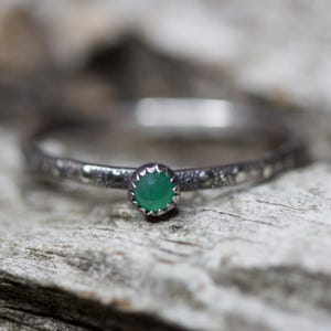 May include: A silver ring with a textured band and a small, round, green gemstone.