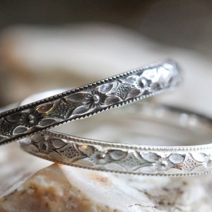 May include: Two silver rings with intricate floral designs. The rings are stacked on top of each other.
