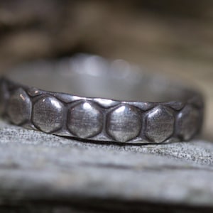 May include: A silver ring with a textured hexagonal pattern. The ring is made of metal and has a polished finish.