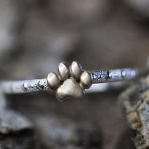May include: A silver ring with a gold paw print charm. The ring is decorated with small silver beads.
