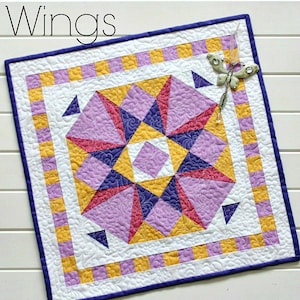 May include: A purple, yellow and pink quilt block with a starburst design. The quilt block is surrounded by a border of yellow and purple stripes. The quilt block is titled "Wings".