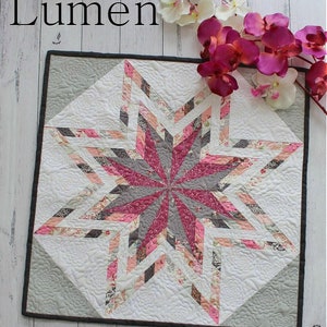 May include: A gray and white quilt with a pink and gray star design. The quilt is quilted with a swirl pattern. The quilt is surrounded by pink and white flowers.