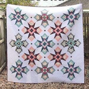 May include: A white quilt with a geometric pattern of stars and diamonds in shades of pink, blue, and gray. The quilt is titled "Hestia".