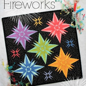 May include: A black fabric quilt with a "Fireworks" title and six colorful star-shaped designs. The stars are in shades of pink, purple, blue, green, and orange.