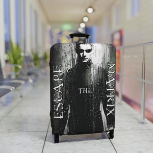 May include: A black and white suitcase cover featuring a graphic of a person wearing sunglasses. The text "ESCAPE THE MATRIX" is printed vertically on the sides of the suitcase cover. The suitcase has a black handle and wheels.