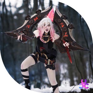 May include: A person in a black costume with a large, ornate weapon. The weapon is dark brown with red accents and a pink blade. The person has white hair with pink highlights and is in a snowy outdoor setting.