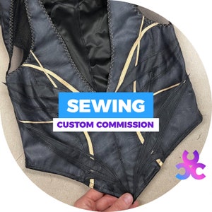 Peut inclure: Gilet en cuir noir avec des détails dorés et des coutures décoratives. Le gilet présente une encolure en V et porte l'inscription "SEWING CUSTOM COMMISSION" sur une bannière bleue et violette.