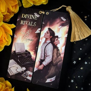 Puede incluir: Dos marcapáginas con fondo oscuro y detalles dorados. El marcapáginas de la izquierda presenta una máquina de escribir y el texto "DIVINE RIVALS Tris & Roman". El marcapáginas de la derecha presenta una pareja de pie de espaldas con un fondo oscuro y detalles dorados.