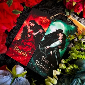 May include: Two bookmarks with romantic illustrations. One bookmark features a couple dancing with the word "Dracula" in red. The other bookmark shows a couple kissing with the words "Van Helsing" in green. Both have a gold tassel.