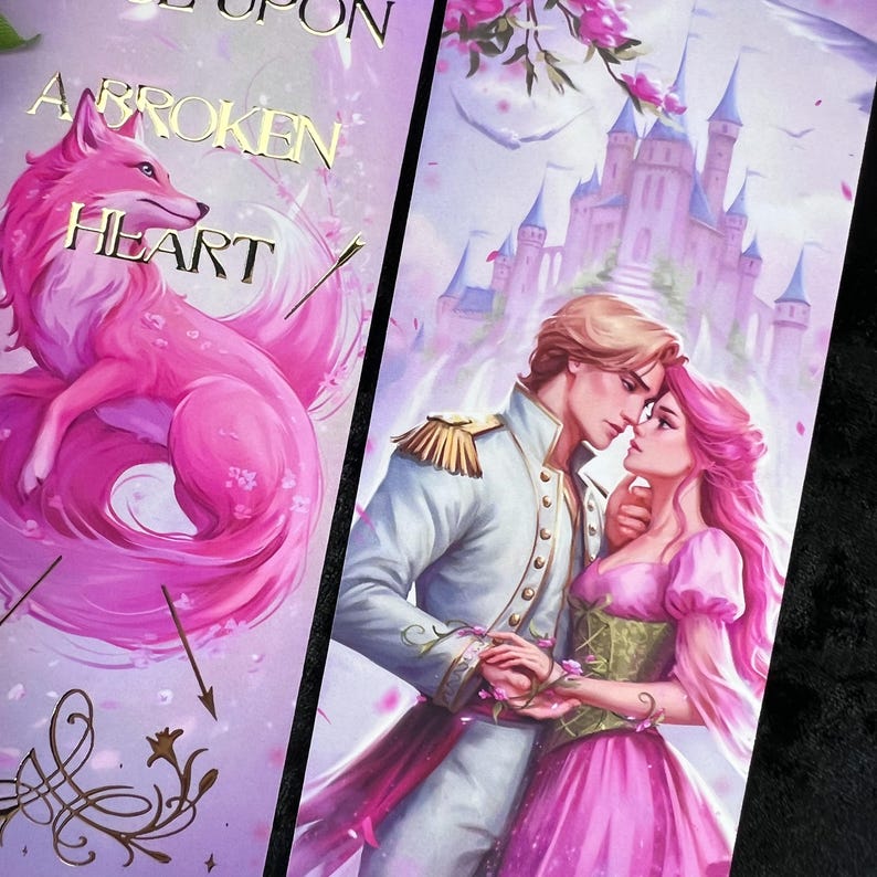 Peut inclure: Deux marque-pages avec des illustrations fantastiques. L'un pr&eacute;sente un renard rose avec le texte "A Broken Heart". L'autre montre un couple devant un ch&acirc;teau. Les deux ont un sch&eacute;ma de couleurs rose et violet.