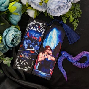 Puede incluir: Dos marcapáginas con un fondo oscuro e ilustraciones coloridas. El primer marcapáginas presenta una serpiente con alas y el texto "The Serpent and the Wings of Night". El segundo marcapáginas presenta una pareja con alas, un fondo azul y un cristal.