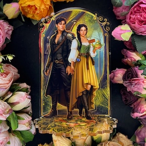 Pu&ograve; includere: Supporto in acrilico raffigurante una coppia fantasy. L'uomo indossa un cappotto nero e una spada. La donna indossa un corsetto verde, una gonna gialla e tiene in mano una rana. Lo sfondo &egrave; una scena di foresta con dettagli dorati.