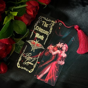 Puede incluir: Un marcapáginas negro y dorado con el texto "The Crimson Moth" y el nombre del autor "Ryne & Gideon". El marcapáginas presenta un diseño de mariposa dorada y una escena de una pareja bailando.