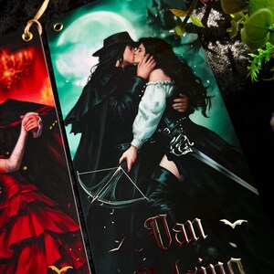 May include: Bookmarks featuring illustrations of characters from a gothic romance. One bookmark depicts a couple kissing in front of a full moon, with the words "Van Helsing" in red. The other bookmark shows a woman in a red dress.
