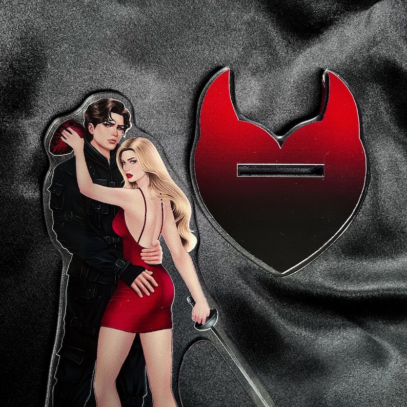 Puede incluir: Una pareja en una pose rom&aacute;ntica, la mujer con un vestido rojo y el hombre con un traje negro, con un recorte en forma de coraz&oacute;n rojo detr&aacute;s de ellos.