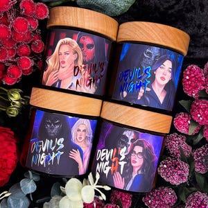 May include: Four candles with wooden lids, each featuring a different character from the book "Devil's Night". The candles are decorated with a dark blue background and the text "Devil's Night" in a white font.
