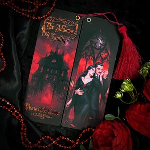 Peut inclure: Deux marque-pages noirs représentant la famille Addams. Un marque-page montre un manoir gothique avec le texte "The Addams Family" et "Morticia & Gomez". L'autre marque-page montre Morticia et Gomez debout devant une fenêtre gothique.