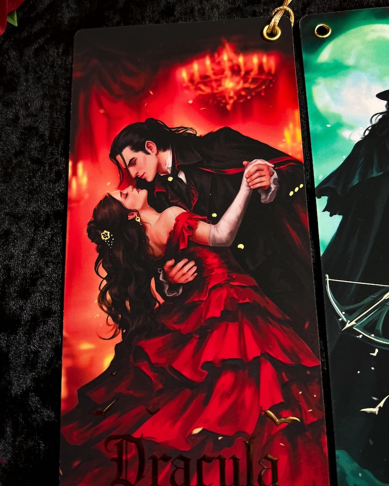 May include: A bookmark featuring a romantic illustration of a couple dancing in a ballroom. The woman wears a red gown, and the man is in a black coat. The word "Dracula" is at the bottom. A gold-colored eyelet is at the top.