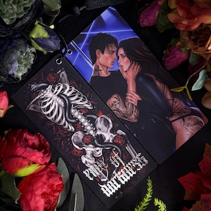 May include: Two rectangular bookmarks featuring dark illustrations. One displays a human skeleton intertwined with a black snake and red roses, with the text 'Rule of Darkness' in gothic font. The other shows a couple embracing with tattoos.