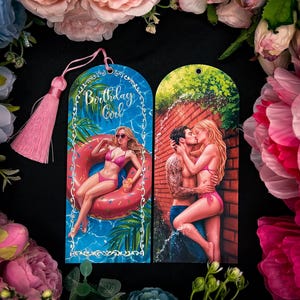 Peut inclure: Deux marque-pages décoratifs avec illustrations. L'un montre une femme en bikini rose sur une bouée avec le texte "Birthday Girl". L'autre représente un couple s'embrassant près d'un mur de briques. Les deux ont des pompons roses.