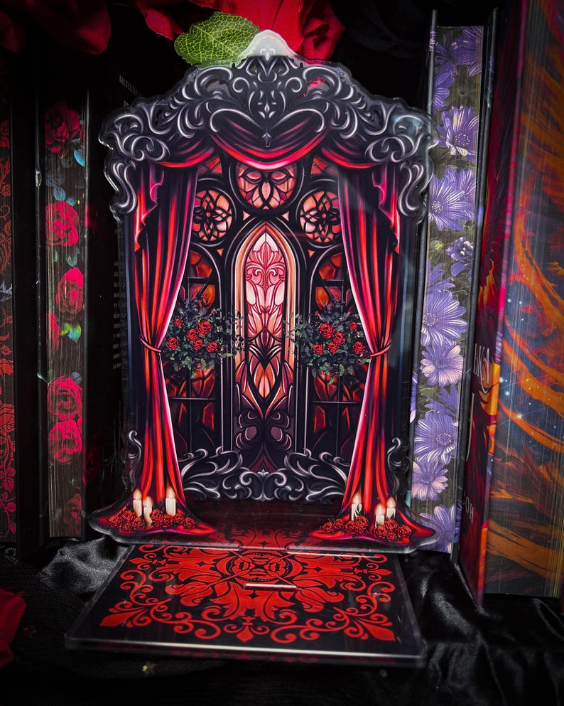 Puede incluir: Expositor g&oacute;tico de acr&iacute;lico, rojo y negro. Presenta un escenario con cortinas rojas, una vidriera y elementos florales decorativos. La base tiene un patr&oacute;n rojo a juego, creando una est&eacute;tica cohesiva.