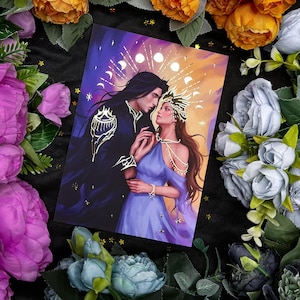 Puede incluir: Una impresión artística de fantasía que presenta a una pareja abrazándose, ambientada en un telón de fondo de elementos celestiales. El hombre lleva una capa oscura con detalles dorados, mientras que la mujer viste un vestido azul fluido. La obra está rodeada de arreglos florales.