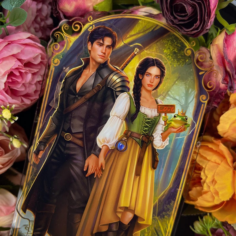 Pu&ograve; includere: Un ciondolo in acrilico a tema fantasy, raffigurante un uomo e una donna in abiti medievali. La donna tiene in mano una rana con una corona e un cartello con la scritta "Love". Lo sfondo &egrave; una scena di foresta con un bordo dorato. Circondato da fiori.