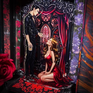 Puede incluir: Pieza de arte acr&iacute;lico que presenta a un hombre vestido de negro ofreciendo una rosa roja a una mujer con un vestido rojo. El fondo incluye un dise&ntilde;o de ventana g&oacute;tica con cortinas rojas y detalles florales. La base tiene un patr&oacute;n ornamental rojo y negro.