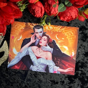 May include: A romantic illustration of a couple in a dramatic setting. The man is wearing a black suit and a white mask, while the woman is wearing a white dress with a red sash. The background is a golden-orange colour with a hint of smoke.