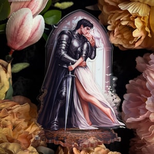 May include: An acrylic standee featuring an illustration of a dark-haired figure in black plate armour holding a sword, embracing a figure with white hair in a long white dress. The figures are positioned within a gothic archway frame.