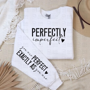 May include: White sweatshirt with the text "PERFECTLY imperfect" and "you are PERFECT EXACTLY AS you are" in black. A black heart graphic is included. A tan hat is in the background.